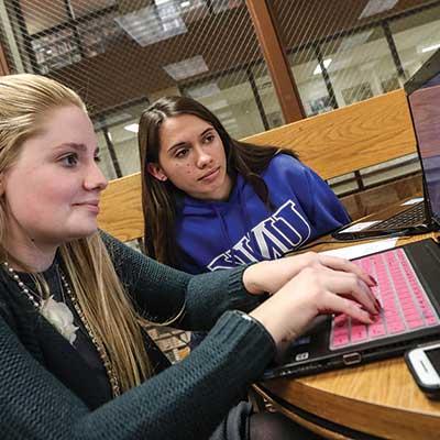 two students sit in front of a laptop